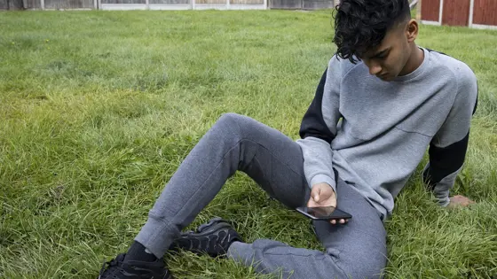 Teenage boy sat on the grass looking at his phone