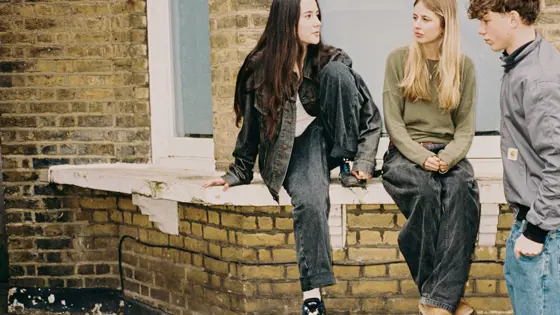 Two teenage girls and a teenage boy sat on a wall outside
