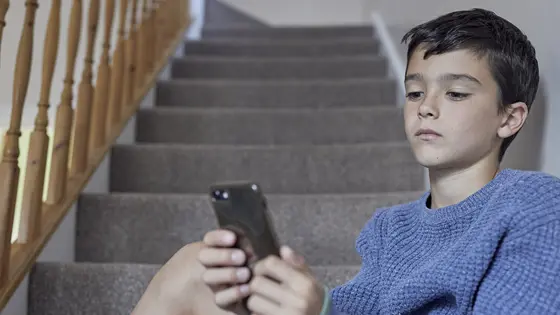 Young boy sat on the stairs looking at his phone