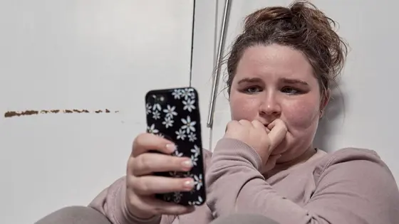A young person sitting on the floor and looking at their phone