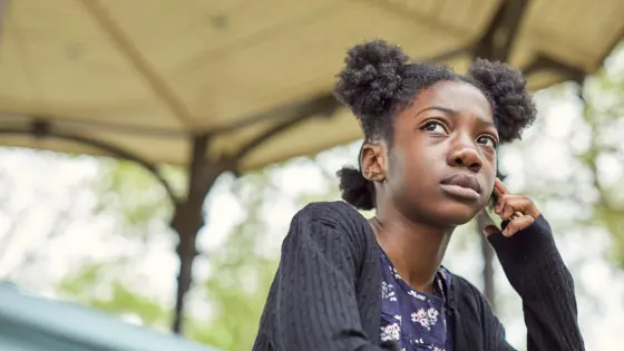 Photo of a teenager standing outside on their phone.